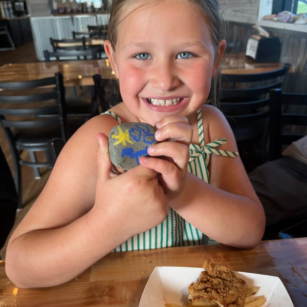Young girl smiling and holding a painted rock at Porch Chair BBQ