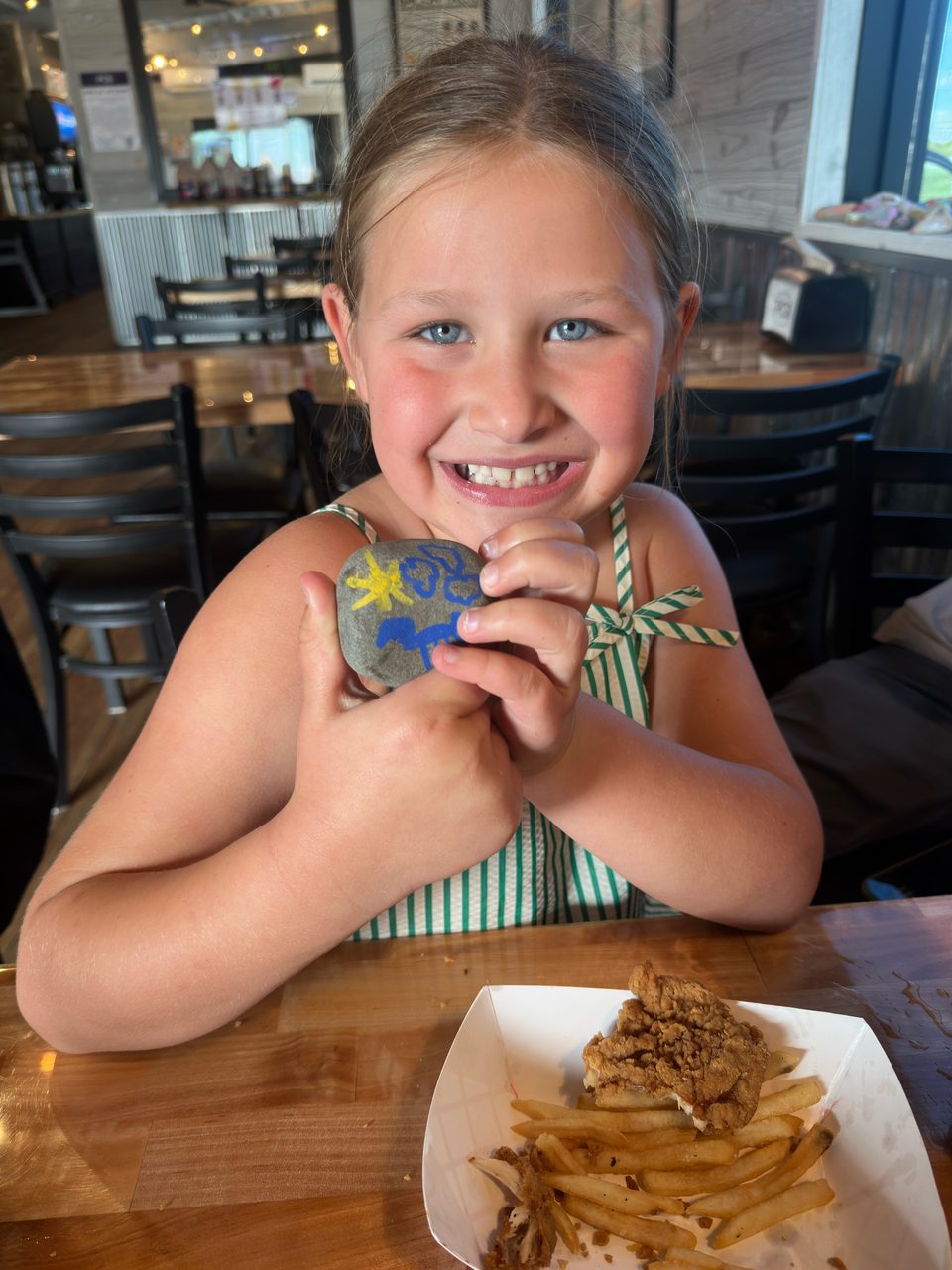 Young girl smiling and holding a painted rock at Porch Chair BBQ